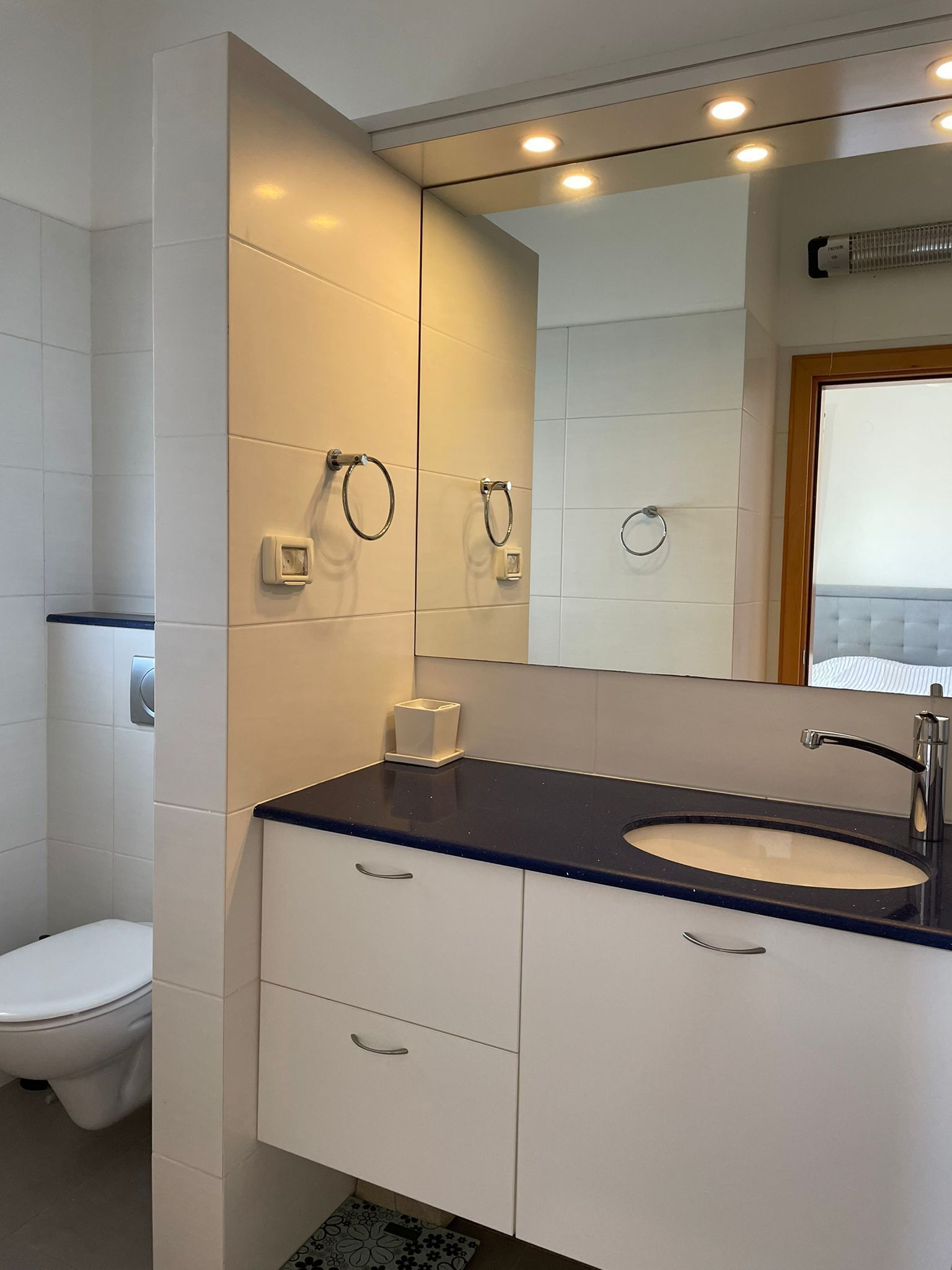 A modern bathroom with a white toilet, a sink with a dark countertop, and a mirror with a wooden frame.