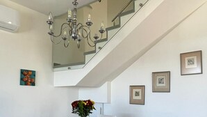Un espace repas avec une table en bois, des chaises blanches, un lustre et un escalier.