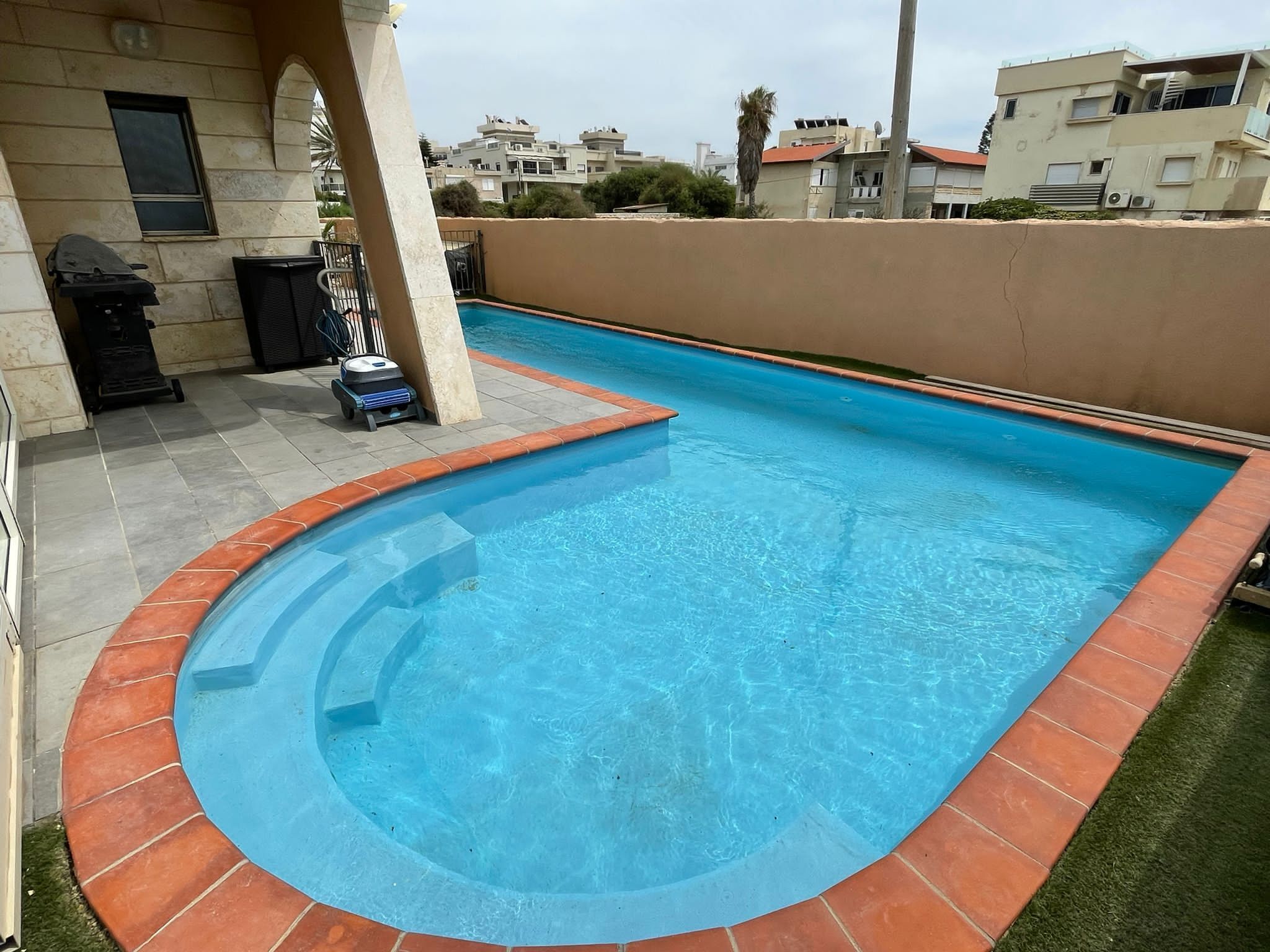 Una piscina rectangular con borde curvo, rodeada por un muro de ladrillo bajo.