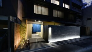 A modern building with a well-lit entrance, a wooden fence, and a small garden area. - Kyoto Machiyado Shijokarasuma (Kyoto)