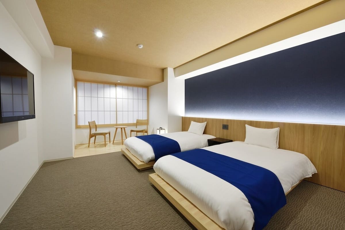 A hotel room with two beds, a TV, a desk, and a large window.