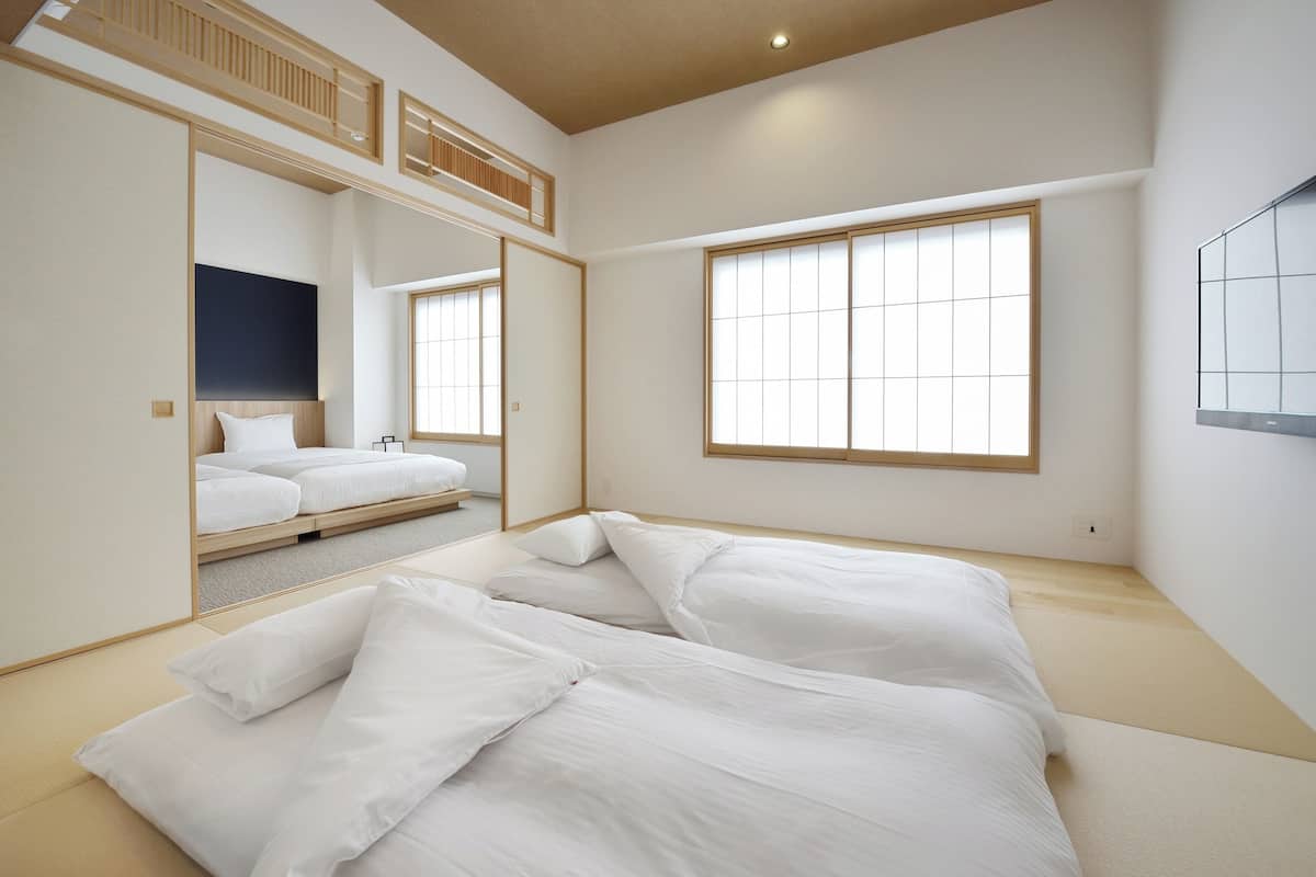 A minimalist Japanese-style bedroom with tatami flooring, a low platform bed, and a large window.