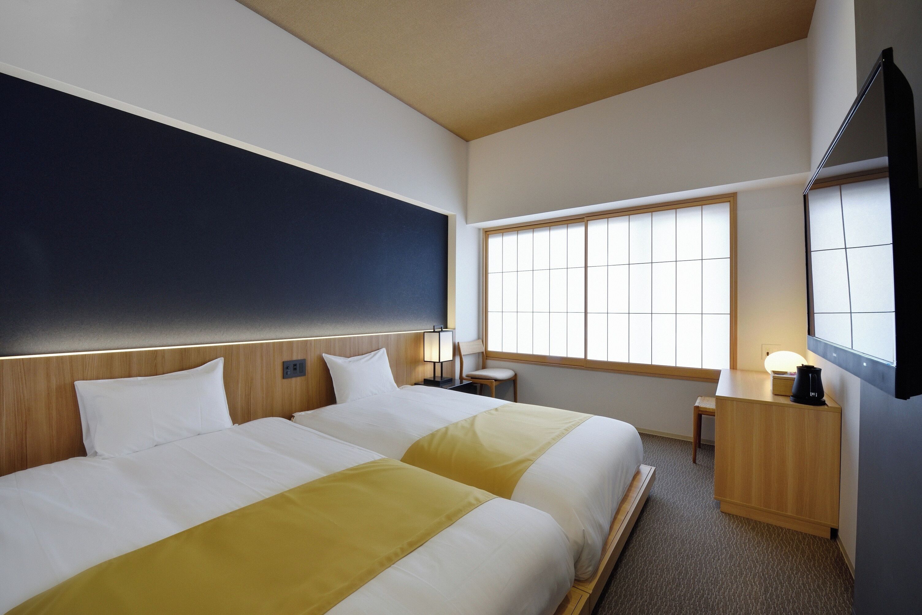 A hotel room with two beds, a large window, a desk, and a TV.