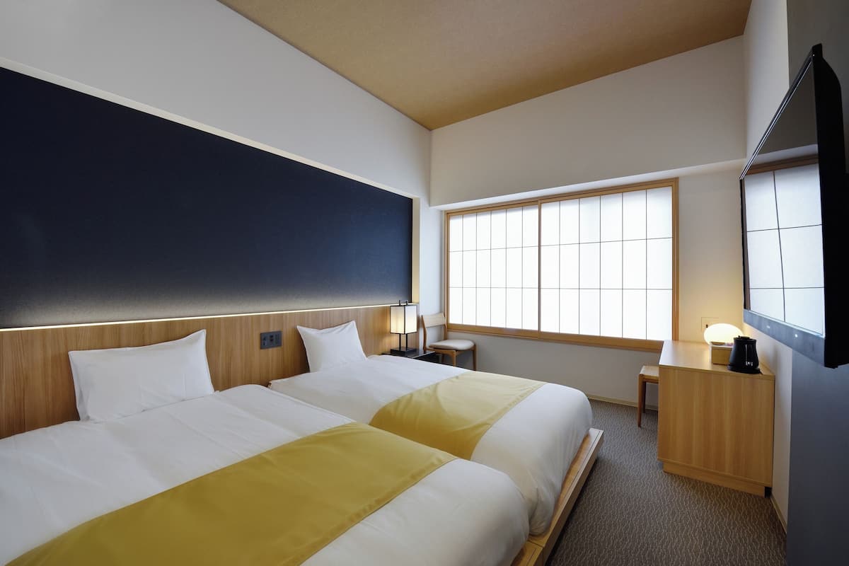 A hotel room with two beds, a large window, a desk, and a TV.
