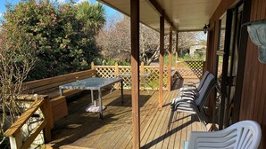 Une terrasse en bois avec une table et des chaises, un banc et un espace abrité délimité par une clôture à treillis.