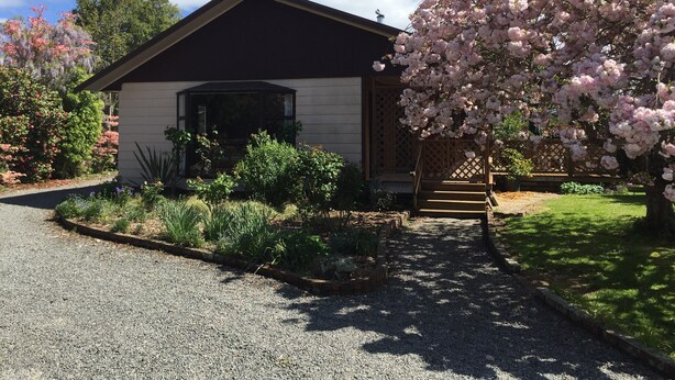 Une maison avec une allée en gravier, un porche en bois et un cerisier en fleurs.