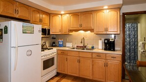 A kitchen with wooden cabinets, a refrigerator, stove, microwave, sink, and a coffee maker. - Cooperstown Baseball Rentals - Dugout 2 (Oneonta)
