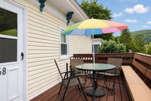 Eine Terrasse mit Glastisch und Stühlen, einem bunten Sonnenschirm und einer weißen Tür mit der Nummer 48.