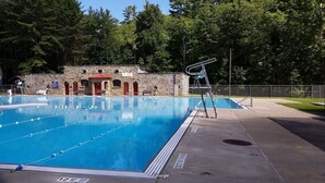 A swimming pool with lane dividers, a lifeguard chair, and a stone building with red doors in the background. - Cooperstown Baseball Rentals - Dugout 2 (Oneonta)