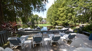 A wooden deck with white lounge chairs and a view of a lake with boats. - Sacino Condo Withlacoochee Rainbow River (Dunnellon)