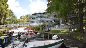 A marina with several boats docked, a wooden dock, and a building with balconies in the background. - Sacino Condo Withlacoochee Rainbow River (Dunnellon)