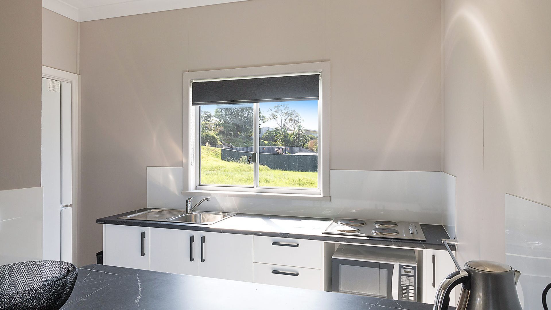 A compact kitchen with a window, a sink, a microwave, and cabinets.