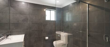A modern bathroom with dark tiles, a glass shower enclosure, a white sink, and a toilet.