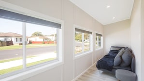 Ein Schlafzimmer mit großen Fenstern, einem Bett und Blick auf eine Straße und Häuser.