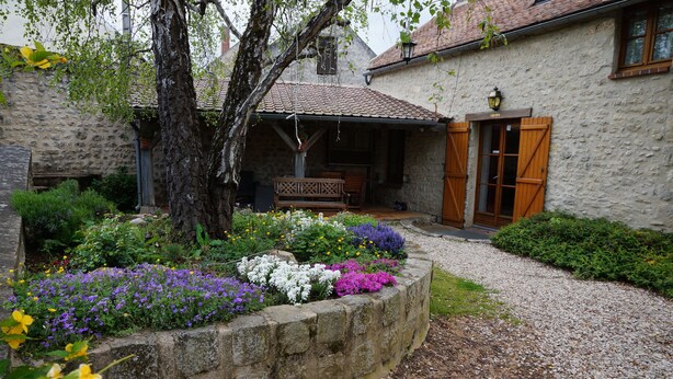 Un bâtiment en pierre doté d’un patio couvert, d’un banc en bois et d’un chemin de gravier.