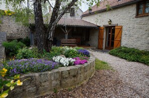 Un edificio de piedra con un patio cubierto, un banco de madera y un camino de grava.
