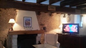 Une pièce chaleureuse avec une cheminée en pierre, une télévision et une table.