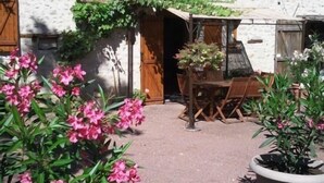Une cour avec une table et des chaises en bois, entourée de murs blancs et d’une porte en bois.
