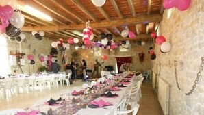 Une salle de banquet avec de longues tables dressées pour un événement formel, décorée de ballons et recouverte de nappes blanches.