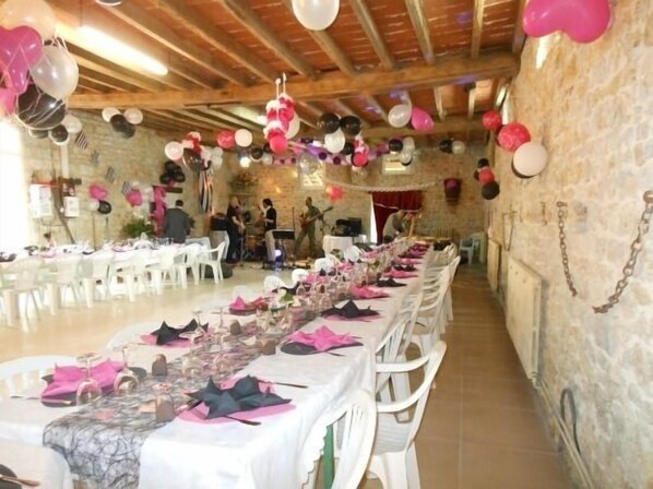 Un salón de banquetes con largas mesas dispuestas para un evento formal, decorado con globos y manteles blancos.