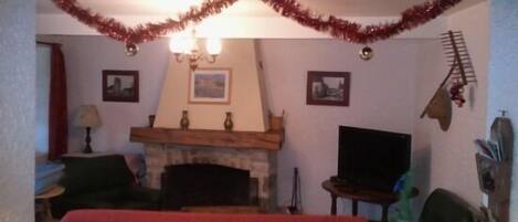 A cozy living room with a fireplace, a television, and a Christmas tree.