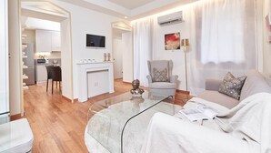 Una sala de estar moderna con una mesa de centro de vidrio, un sofá, una silla y un comedor con cocina al fondo.