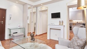 Una sala de estar moderna con una mesa de centro de vidrio, un sofá, una chimenea y una cocina al fondo.