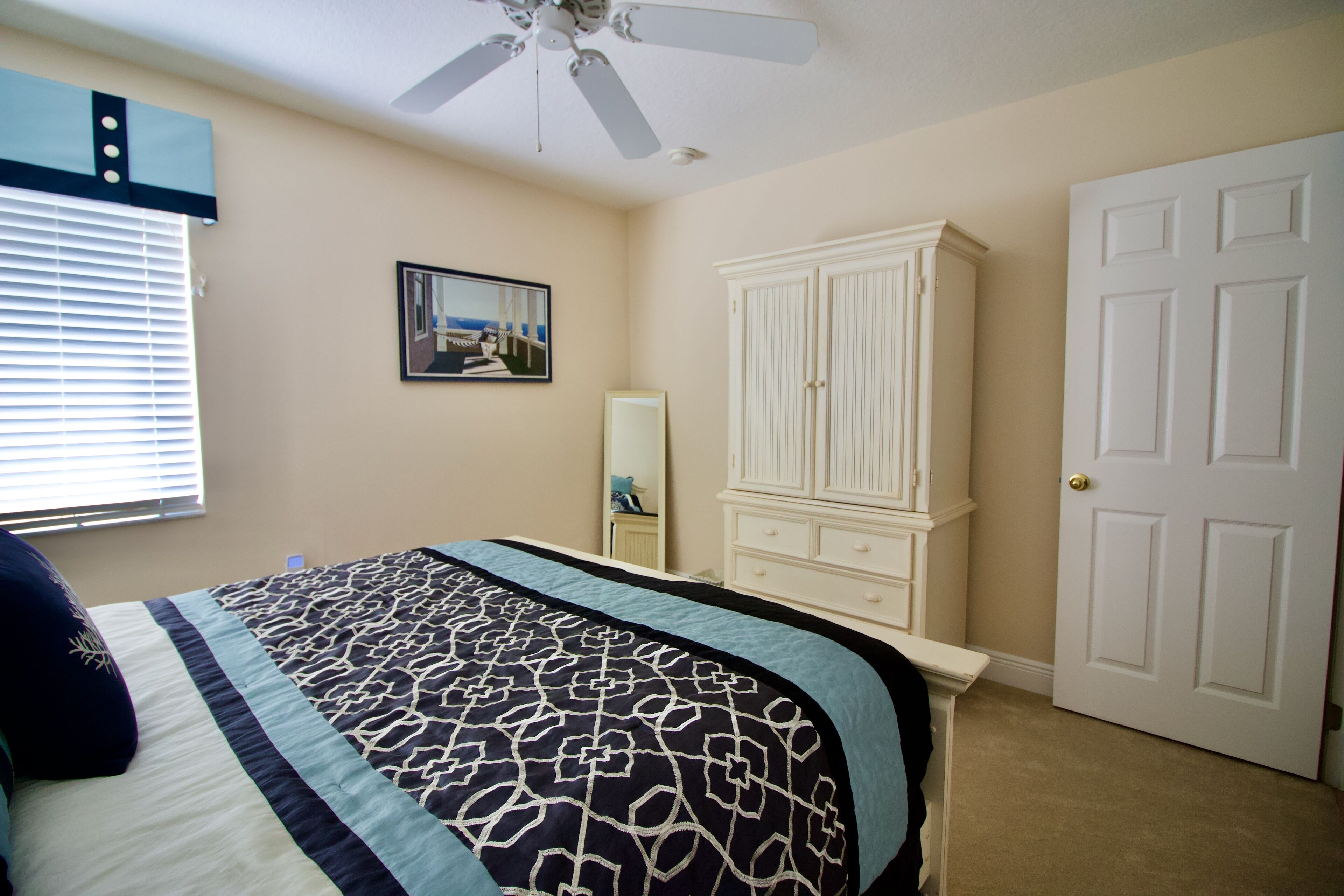 Une chambre à coucher comprenant un lit, un ventilateur de plafond, une armoire, une porte et une fenêtre avec des stores.