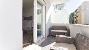 A balcony with a sliding glass door, wicker furniture, and a view of a building in the background. - New and elegant central apartment with box (Alghero)