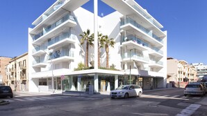 A modern multi-story building with balconies, a glass storefront, and palm trees. - New and elegant central apartment with box (Alghero)
