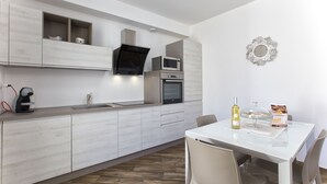 A modern kitchen with built-in appliances, a dining table with chairs, and a decorative wall piece. - New and elegant central apartment with box (Alghero)