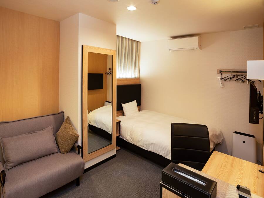 A hotel room with a bed, a sofa, a desk, a mirror, and a TV.