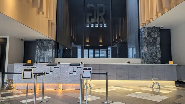 A modern reception area with a marble counter, a large 'QR' sign, and a check-in kiosk.