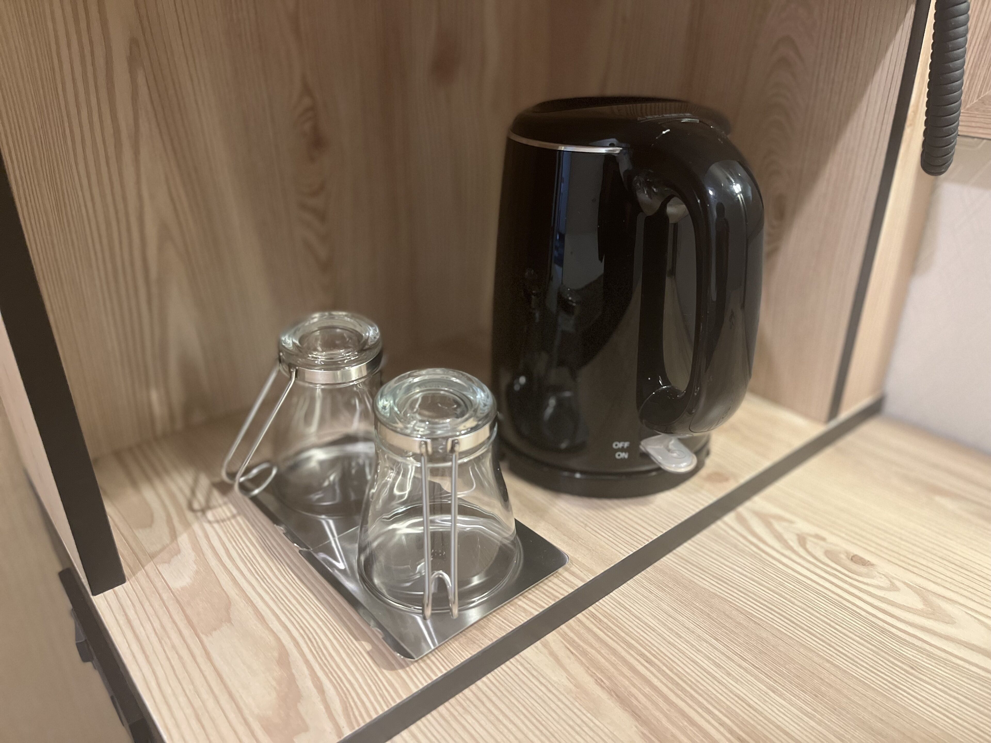 Un estante de madera con una cafetera negra y dos recipientes de vidrio transparente.