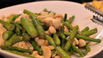 A white plate with cooked asparagus and white beans, a pair of tongs, and a blurred background.