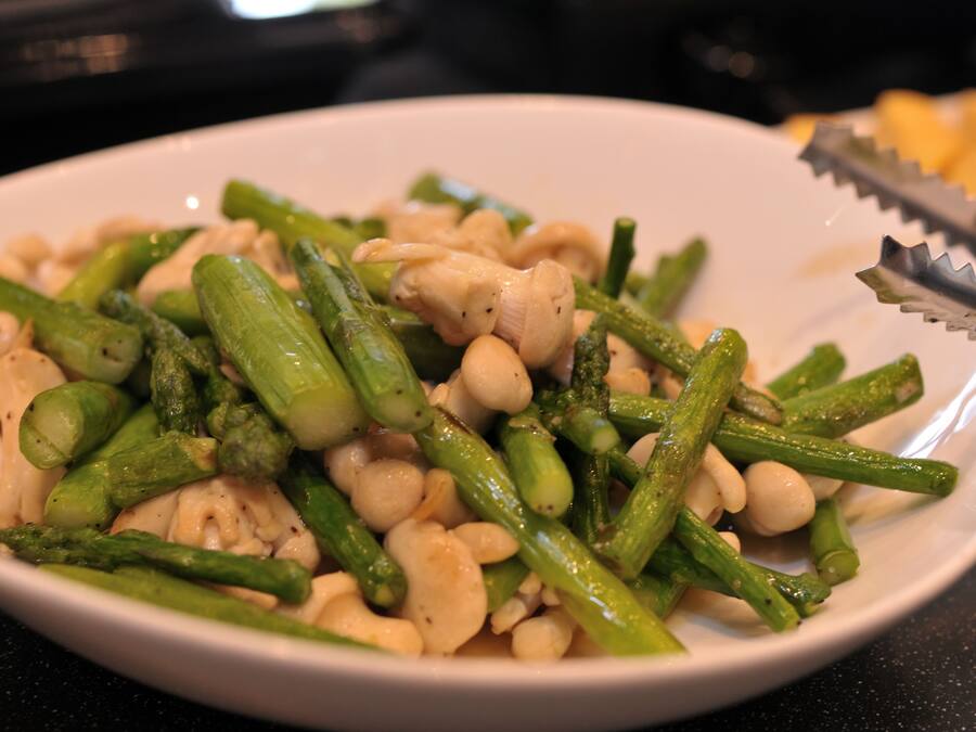 A white plate with cooked asparagus and white beans, a pair of tongs, and a blurred background.