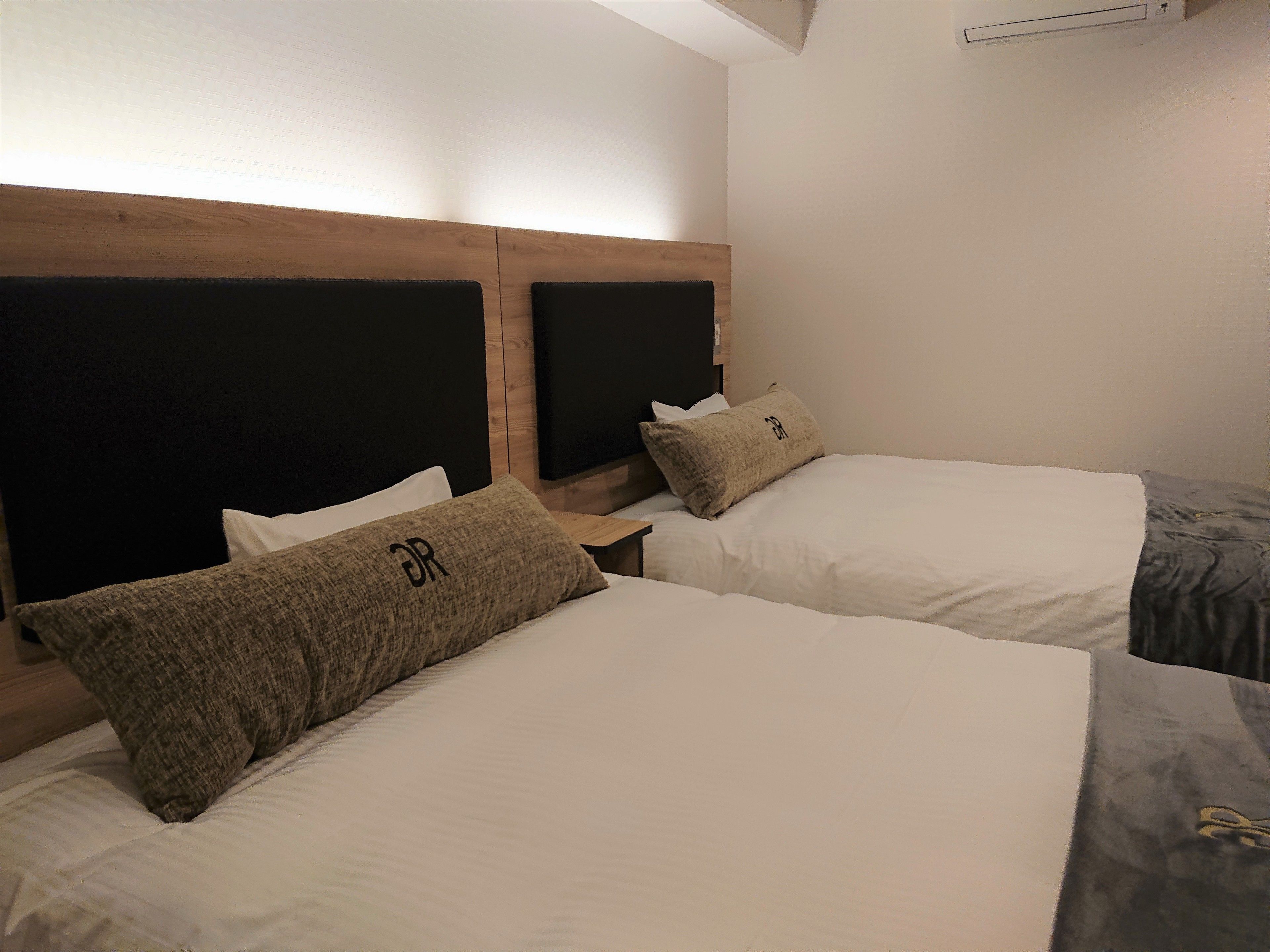 Habitación de hotel con dos camas, cada una con cabecero de madera y almohada con un logo.