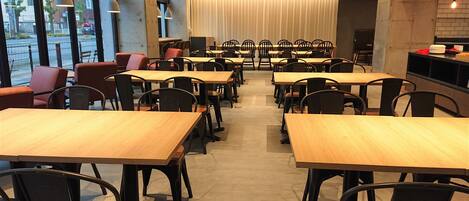 A spacious dining area with multiple tables and chairs, large windows, and a modern interior design.