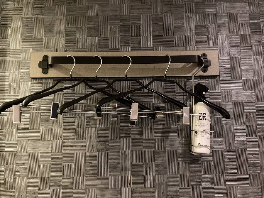 A wall-mounted drying rack with multiple hooks and a bottle of hand sanitizer.
