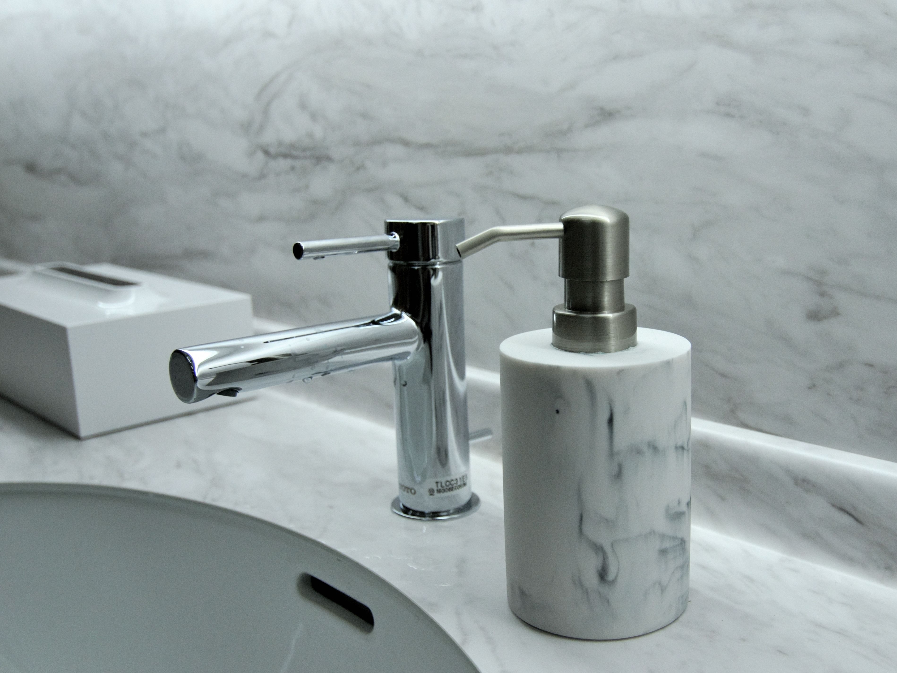 A bathroom sink with a marble countertop, a chrome faucet, and a soap dispenser.