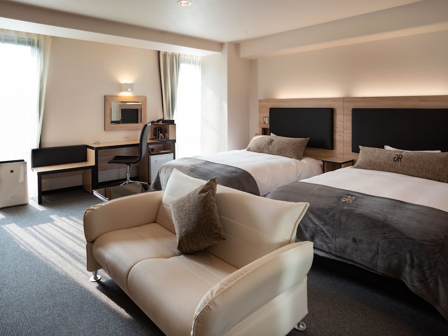 A hotel room with two beds, a desk, a chair, and a sofa.