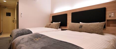 A hotel room with two beds, each with a headboard and pillows, a bedside table, and an air conditioning unit on the wall.