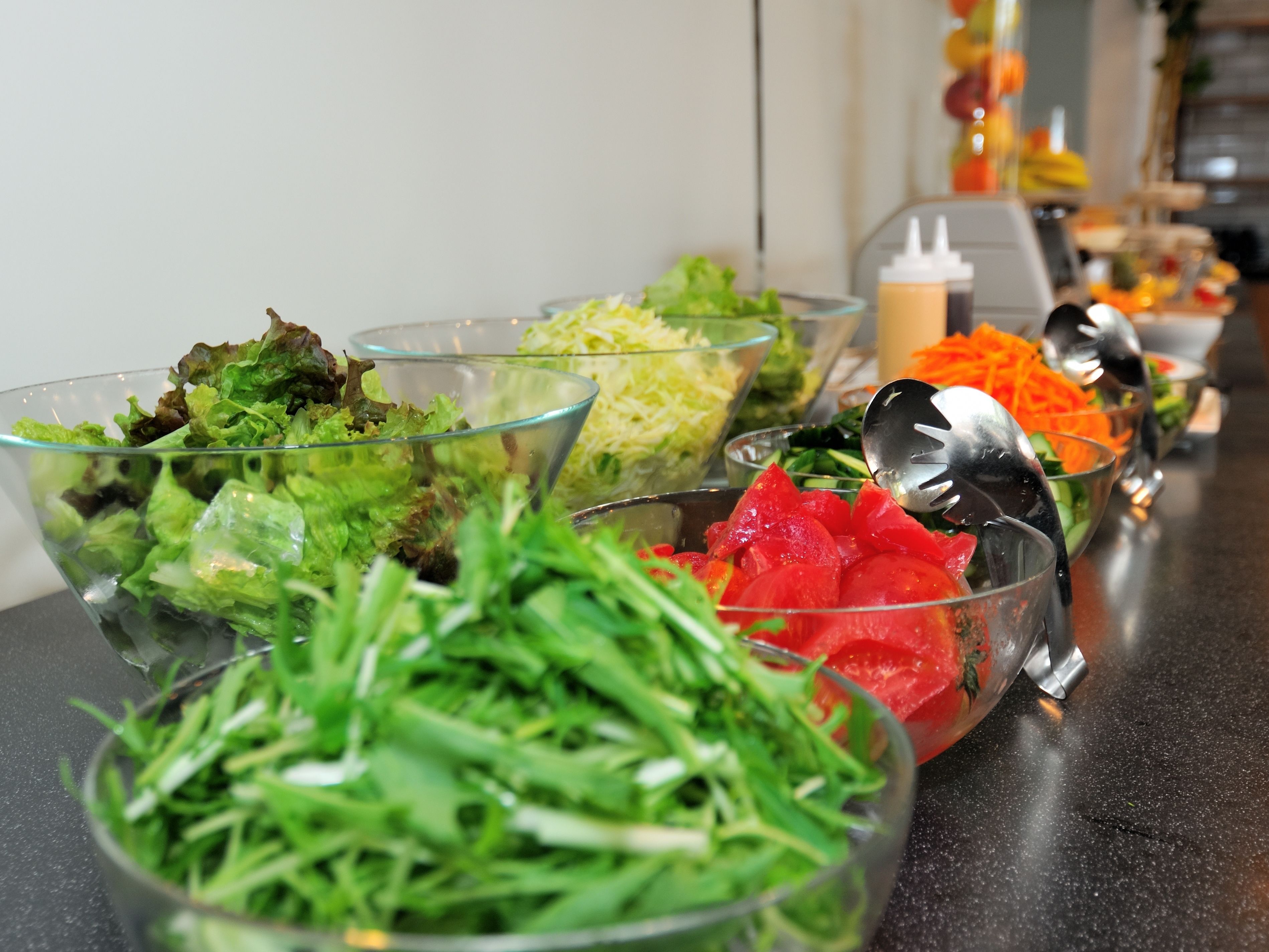 Una mesa de bufé con ensaladas variadas en recipientes de vidrio transparente.