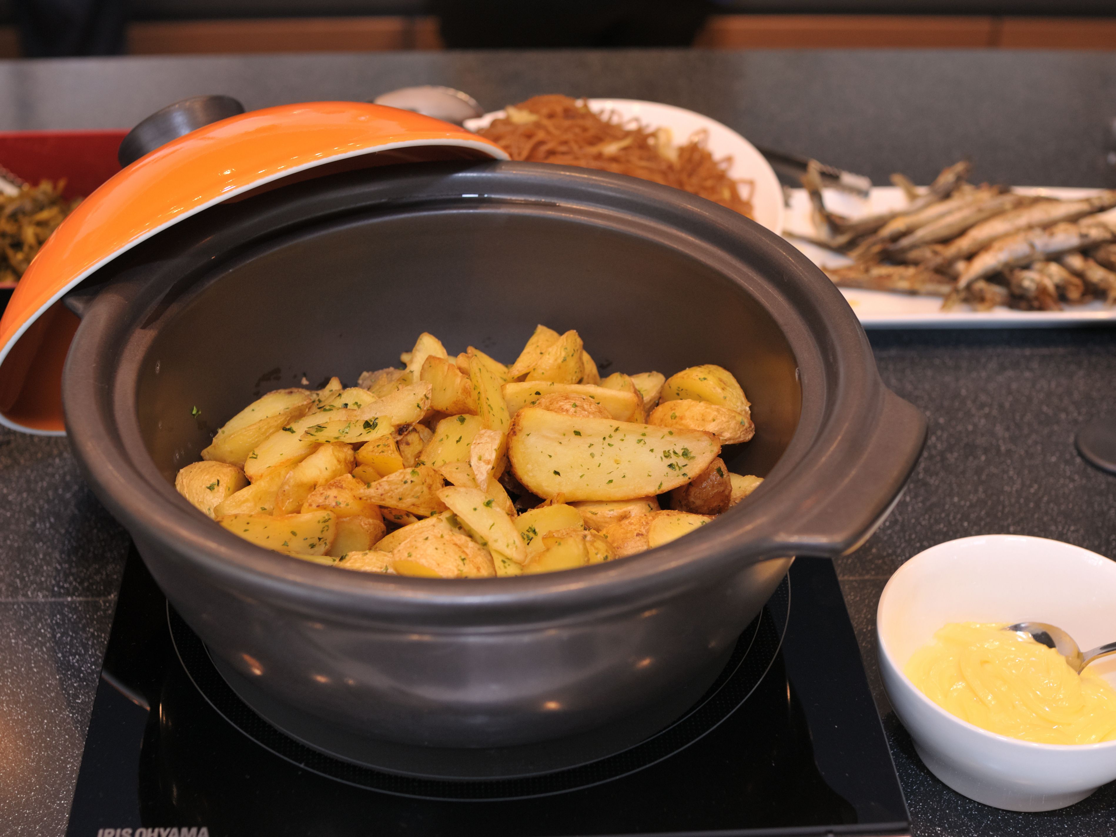 A slow cooker with cooked potatoes and a bowl of sauce on a kitchen counter.