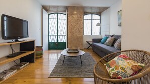 Een moderne woonkamer met een flatscreen televisie, een bank met gestreepte kussens, een rieten fauteuil en een groot raam met uitzicht.