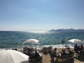 A beachside setting with sun loungers and umbrellas, a clear view of the sea, and distant mountains.