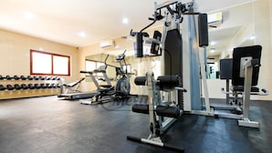 Un gimnasio con diversos equipos de ejercicio, un aire acondicionado instalado en la pared y una ventana con persianas.