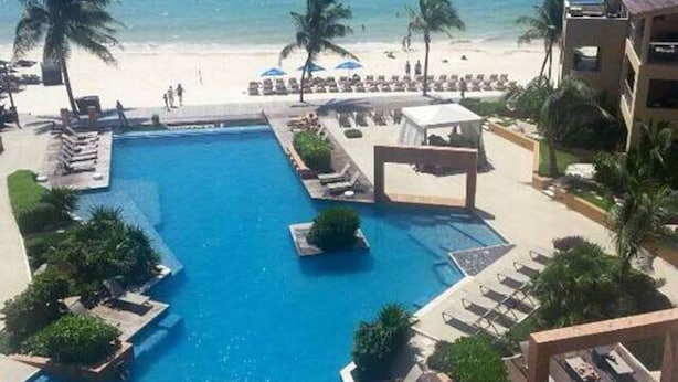 Un resort con piscina central, zonas de descanso y vista al mar.