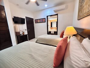 A hotel room with two beds, a bedside table with a lamp, a mirror, and a wall-mounted TV. - Sea Style Ocean View 2 Bedroom Condo, 2nd Floor at El Faro by DPM (Playa del Carmen)