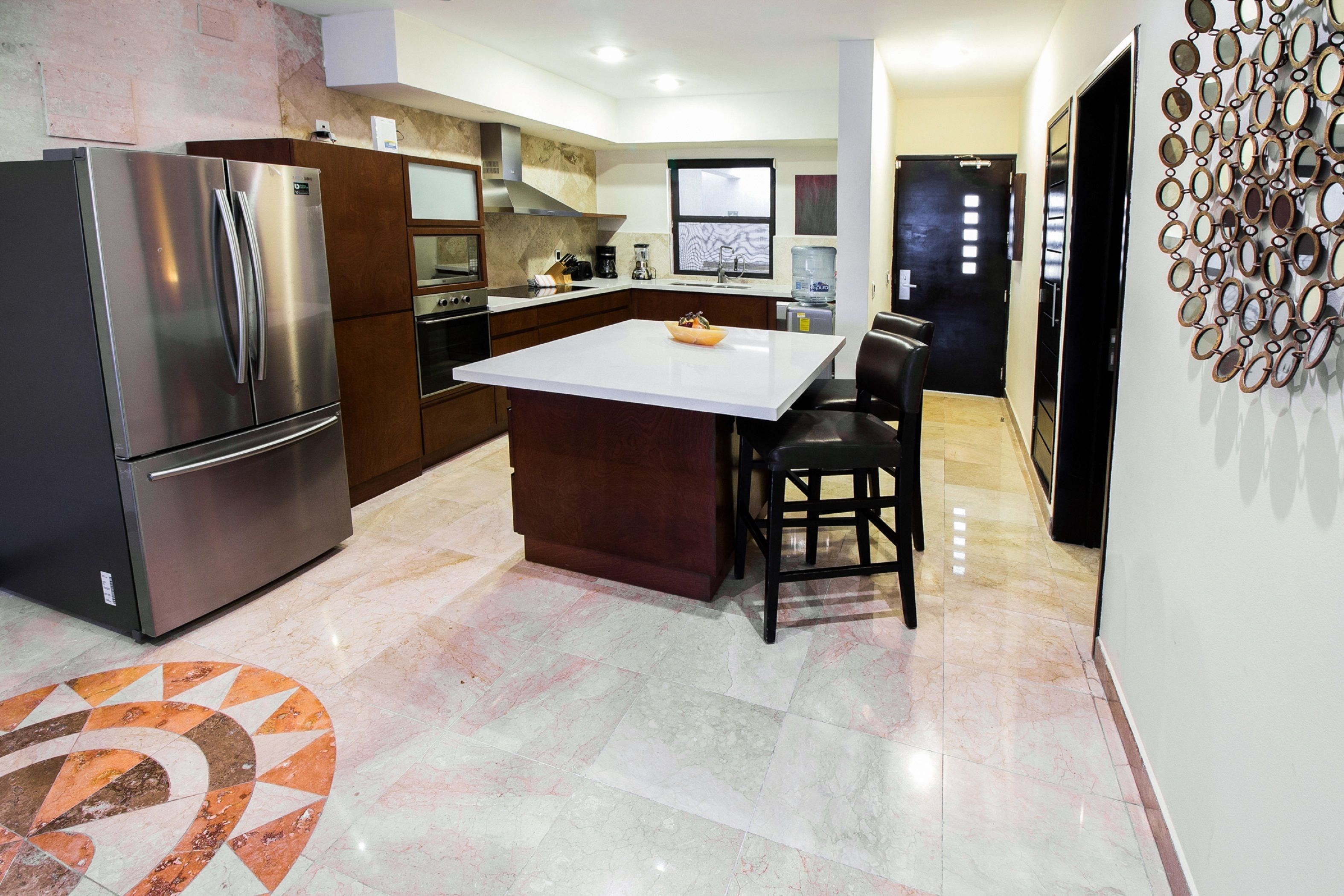 A modern kitchen with a stainless steel refrigerator, a large island, and a water dispenser.